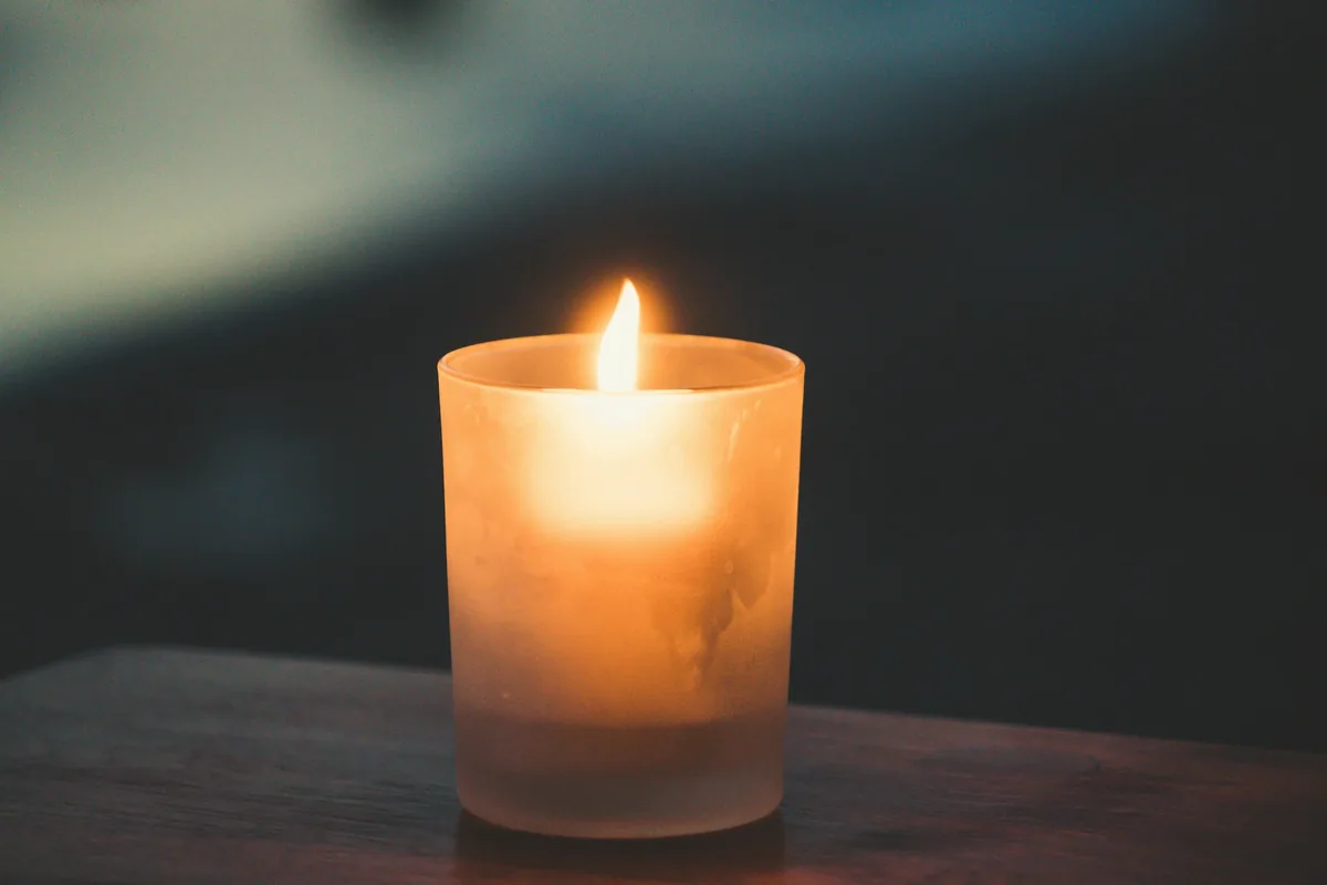 Flamme d’une bougie dans un verre, sur une table sombre