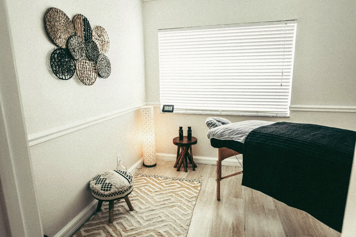 Petite salle de séance : table habillée d’un drap sombre, tabouret, lampe et fenêtre à stores