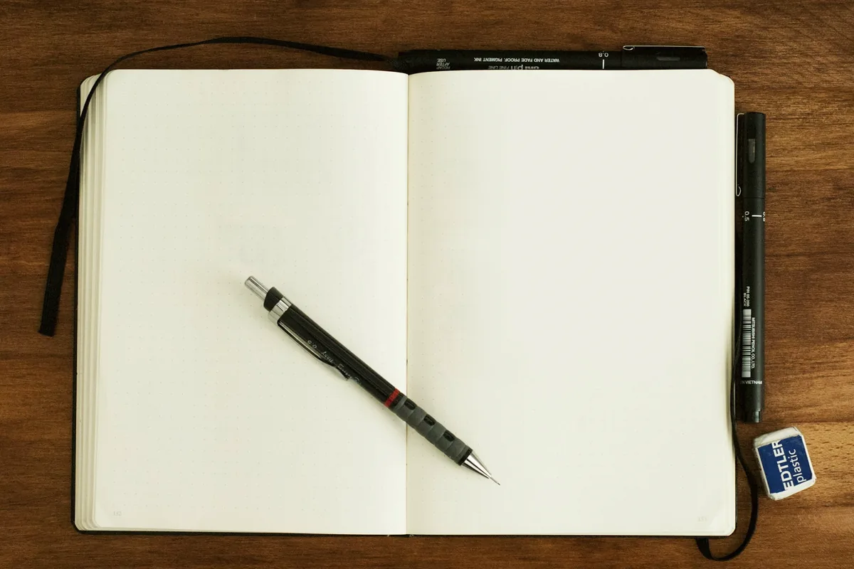 Carnet ouvert aux pages vierges et crayon posés sur une table en bois